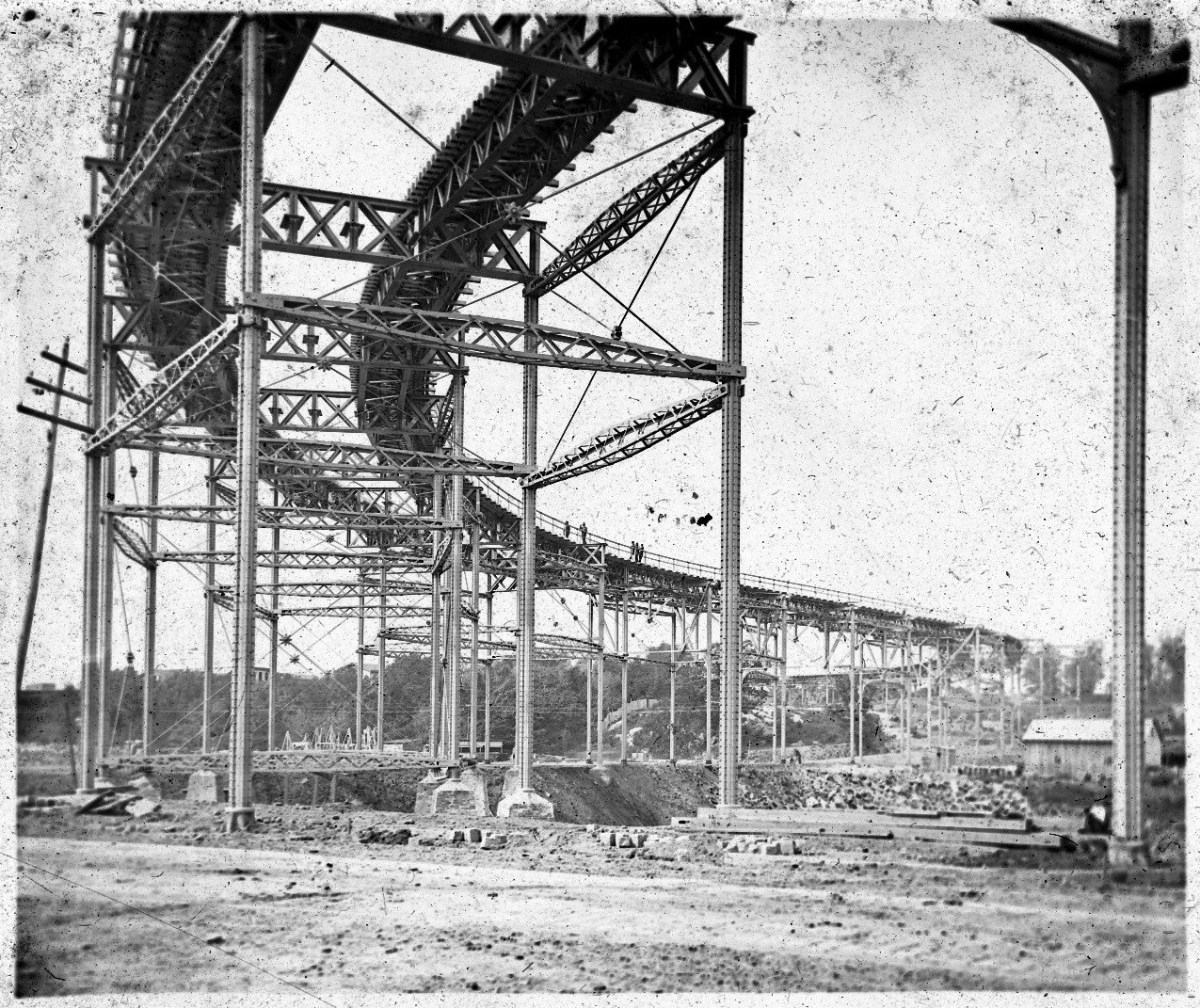 The bare iron towers of the 110th Street curve under construction in 1879: tall riveted columns on masonry pedestals, lattice struts and diagonal rods, with workmen on the deck.