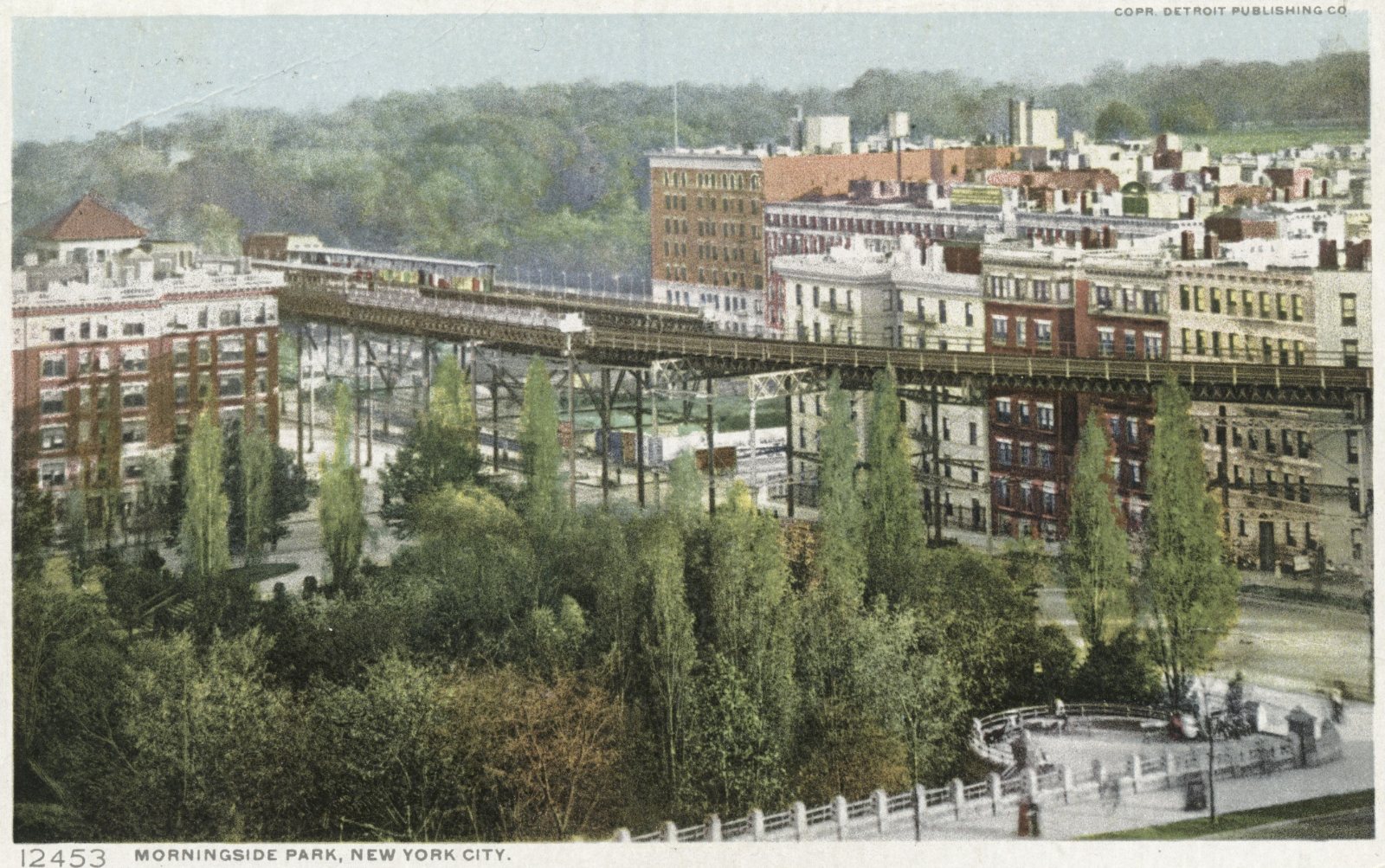 Coloured postcard of the Ninth Avenue El running broadside along Eighth Avenue past Morningside Park, with a train on the structure and apartment buildings behind.