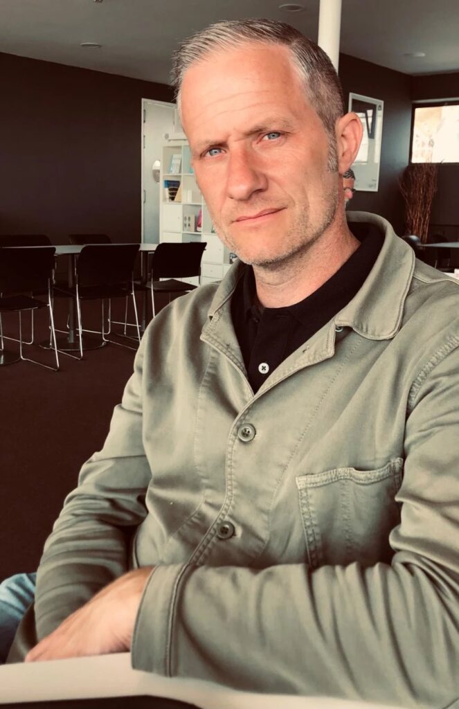 James Walters, in a green jacket, seated at a table and looking at the camera.